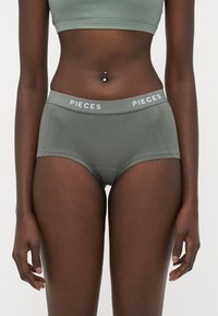 Zelena pamučna hipster gaćice s mekim pojasom, s imenom branda "PIECES" u bijelom slovu. Glatka tekstura, minimalistički dizajn.