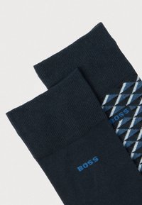 Meias azuis-marinho com padrão riscado texturizado na parte superior e design geométrico azul e branco na parte inferior. Logótipo "BOSS" em azul.