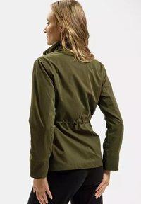 Oliwkowa kurtka z dopasowaną talią, długimi rękawami i stójką. Gładki materiał z subtelnym połyskiem i bez widocznych elementów metalowych.