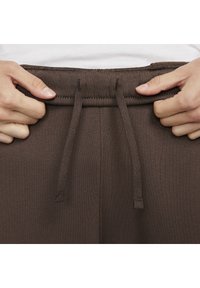 Brun dragsnöre i midjan på träningsbyxor, med en texturerad tyg, justerbara band och platt söm synlig i kanterna.