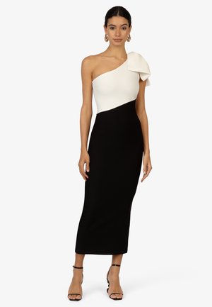 Eén-schouder jurk, witte bovenkant met een strikdetail, zwarte aansluitende rok, soepel materiaal, enkelband hakken. Eenvoudige, elegante silhouet.