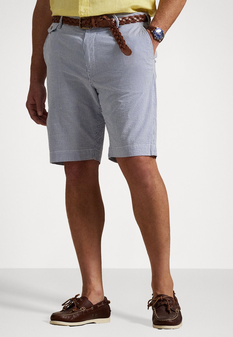 Chino à rayures pour hommes en bleu et blanc avec une coupe classique. Porté avec une ceinture tressée marron et des chaussures bateau marron. Texture lisse.