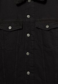 Veste en jean noire avec boutons-pression argentés, deux poches à rabat devant et un col en sherling noir.