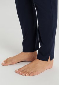 Navyblauwe katoenen broek met zijsplitten aan de onderkant, aansluitend bij de enkels, gedragen met blote voeten en een lichte nagellak.