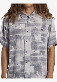 Camisa de botones de manga corta en una tela gris clara con un patrón abstracto en gris oscuro, con un bolsillo en el pecho y un corte relajado.
