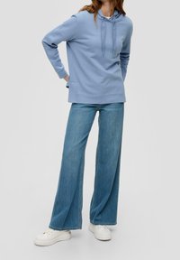 Sudadera con capucha de color azul claro en tela suave con bolsillo frontal; combinada con jeans de pierna amplia en lavado claro y zapatillas blancas.
