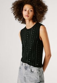 Μαύρο πλεκτό τοπ χωρίς μανίκια με κάθετη ρίγα και διακριτικές διακοσμήσεις με παγιέτες. Διαθέτει στρογγυλή λαιμόκοψη και ίσια τελείωμα. Φοράται με ανοιχτόχρωμα τζιν σορτς.