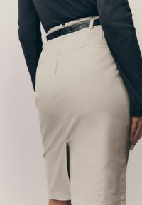Beige skræddersyede shorts med en glat tekstur, der har sidelommer og et sort struktureret bælte i taljen. Nærbillede af bagv,.