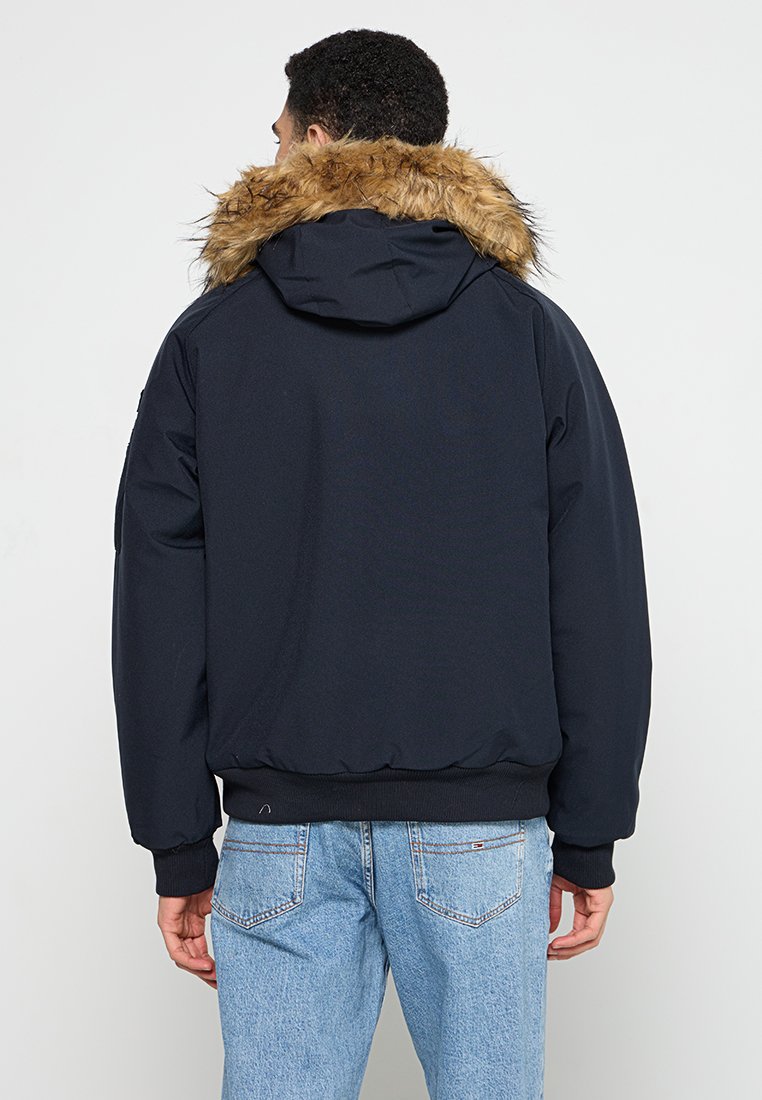 Veste à capuche marine avec un col en fourrure synthétique, des poignets et un ourlet élastiques, et une texture lisse. Caractérisée par une coupe décontractée et un design minimaliste.