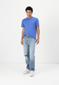 Blå bomulds t-shirt med "TOMMY JEANS" logo, parret med lyseblå distressed denim jeans og hvide sneakers. Enkelt, afslappet outfit.