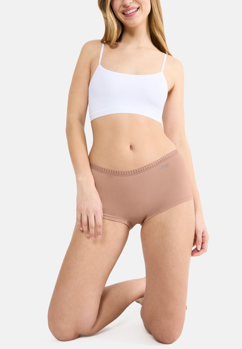 Beige boyshorts med texturerad midjeresår, i kombination med en vit bralette med tunna axelband. Slät tyg, minimalistisk design.