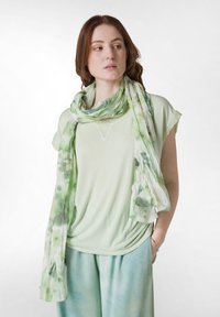 Lys grøn t-shirt med korte ærmer, V-hals og draperet design, parret med et flydende, akvarel-mønstret grøn- og hvidt tørklæde.