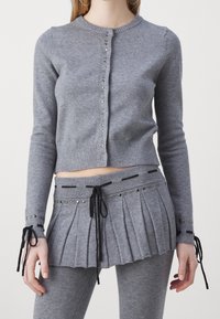 Szary dziergany kardigan z zapięciem na guziki, długimi rękawami i ozdobnymi ćwiekami. W połączeniu z szaroną spódnicą plisowaną z troczkami i ćwiekami.