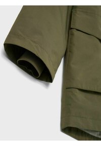 Manche de veste vert olive avec un poignet côtelé et une texture lisse, présentant une coupe droite et une poche partielle visible sur le côté.