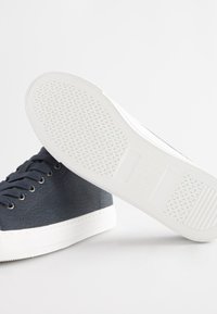 Tumši zili auduma sporta apavi ar reljefu apdari, balta gumijas zolīte ar rakstainu saķeri. Aprīkoti ar apaļām šņorēm un minimālistisku dizainu.