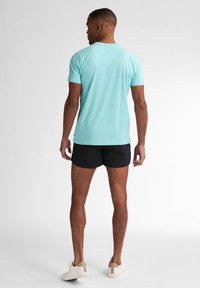 Tricou scurt cu mâneci, de culoare albastră deschisă, din bumbac, asortat cu pantaloni scurți negri și adidași albi cu un accent bej la toc.