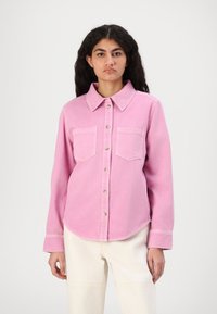 Pink denim shirt with a classic collar, front button closure, and two chest pockets. The fabric has a soft texture with visible stitching details.