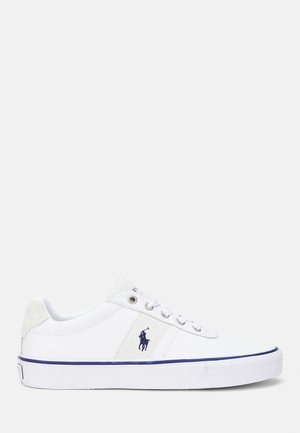 Bílé tenisky s hladkým koženým svrškem, kulatou špičkou, akcenty v námořnické modři a logem na boku. Obsahují šněrování a gumovou podrážku.