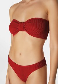 Röd baddräkt i två delar med en texturerad bandeau-topp med rosett och matchande lågt skurna bottoms. Tillverkad av ribbat tyg.