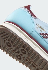 Sneaker-Ferse aus hellblauem und kastanienbraunem Leder, weiße Sohle und braune strukturierte Gummiaußensohle mit Adidas-Logo und detaillierter Nahtarbeit.