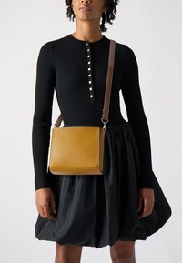 Borsa strutturata in pelle senape con finitura liscia. Presenta una tracolla regolabile marrone e dettagli in metallo argentato.