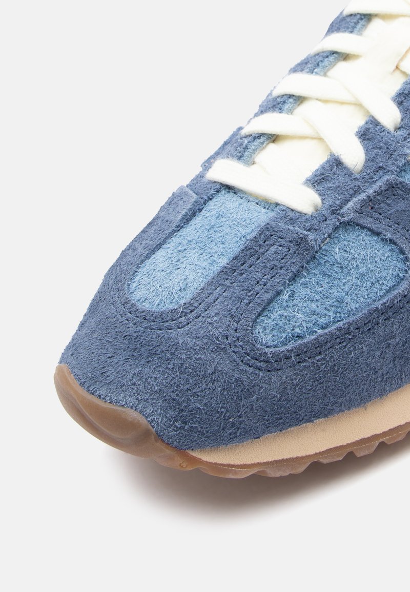 Wildleder- und Textilsneaker in Dunkelblau- und Hellblautönen. Mit einer beigen Sohle und weißen Schnürsenkeln. Strukturiert Oberfläche mit kontrastierenden Paneelen.