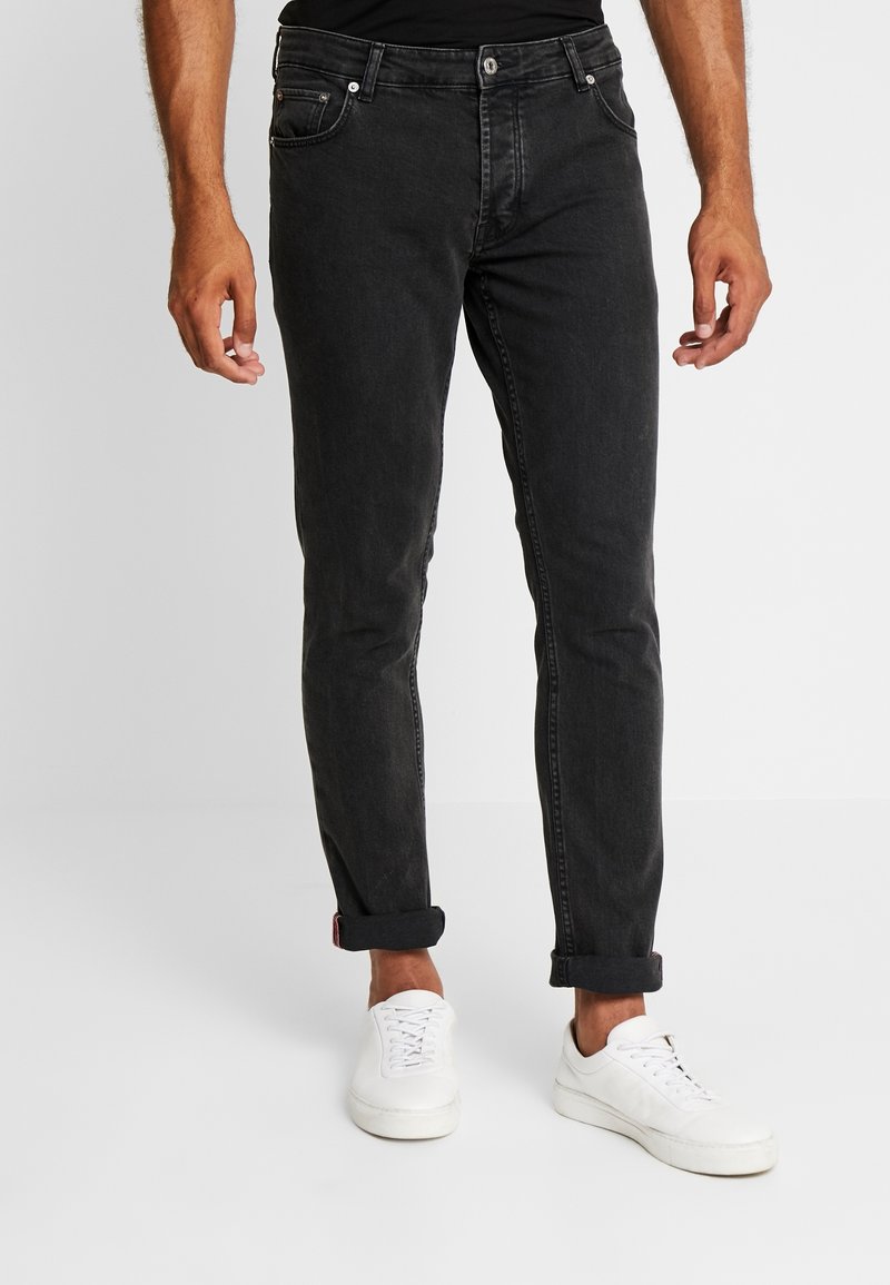 Jeans de mezclilla negra con corte ajustado, que cuentan con cinco bolsillos, un sutil desgaste y dobladillos enrollados, combinados con zapatillas blancas.