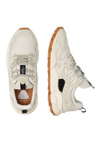 Beige sneakers med ovandel av mesh, texturerade detaljer och svarta inslag. Platta snören och en gummisula med mönstrat grepp.