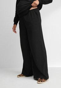 Zwarte wijde broek met een elastische tailleband, gemaakt van een textuurstof. Gescoord met slip-on schoenen met een luipaardprint.