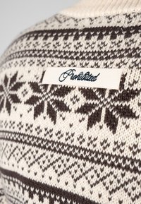 Gros plan sur un tissu tricoté noir et blanc avec des motifs géométriques et une étiquette tissée blanche cousue sur la partie supérieure.