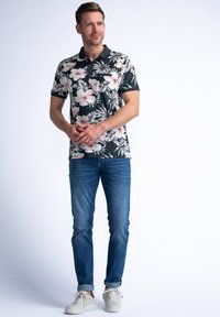 Camisa polo floral con un fondo oscuro que presenta flores rosas y blancas, combinado con jeans azules y zapatillas ligeras. Mangas cortas y cuello.