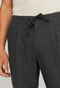 Donkergrijze broek met streepjes en een trekkoord in de taille, gemaakt van zachte stof. Voorzien van zijzakken en een relaxte pasvorm, met accent op de dunne strepen.