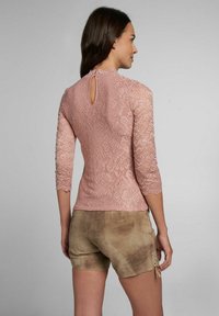 Spitzentop in zartem Pink mit Dreiviertelärmeln, floralem Muster, gewellten Kanten und einem Schlüssel-Loch-Detail am Rücken, kombiniert mit Wildleder-Shorts.