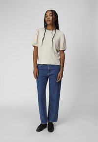 Beige ribbet T-shirt med korte ærmer og pufærmer, parret med blå vide jeans. Sorte sko fuldender outfittet.