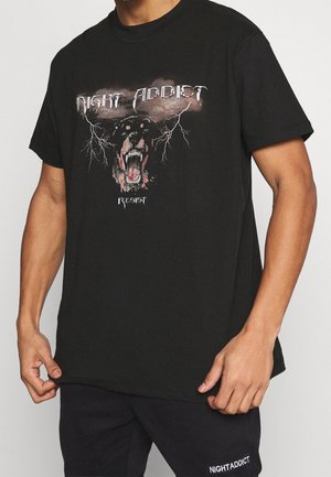 T-shirt in cotone nero con un grande grafico di un cane che ringhia con fulmini, e il testo "NIGHT ADDICT" e "RESIST" in caratteri stilizzati.