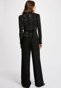 Top nero con texture e motivo verticale, maniche lunghe e spalle imbottite, abbinato a pantaloni neri a gamba larga con vita alta.
