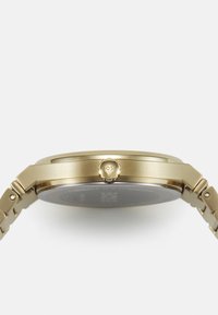 Reloj dorado con caja redonda, corona texturizada y pulsera de eslabones. La esfera presenta un diseño minimalista con una sutil marca.