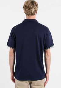 Polo bleu marine à manches courtes avec bordure blanche, un logo discret au dos et un col classique. Tissu en coton doux.