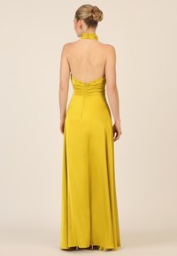 Gelbes Neckholder-Kleid mit eng anliegendem Oberteil, gerafftem Rückenteil und fließendem Rock, der den Boden erreicht, aus glattem Stoff gefertigt.