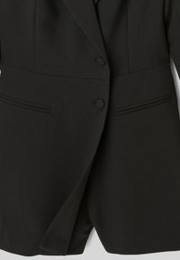 Blazer noir avec une coupe ajustée, présentant deux boutons, des revers étroits et des poches latérales. Texture lisse avec un minimum de détails.
