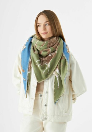 Écharpe en triangle avec des nuances de vert et de bleu, ornée de motifs, à bords frangés et à texture douce, portée sur une veste de couleur claire.