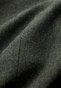 Tejido de un verde oscuro con una superficie suave y difusa, detalles de costura sutiles, mostrando pliegues suaves y un acabado mate.