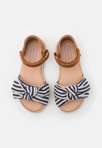 Bruna lädersandaler med en blå och vit randig tygrosett, öppen tå-design och ett slingback-rem. Sulan är av ett platt, ljusfärgat material.