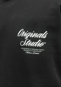 Schwarzer Baumwoll-Sweatshirt mit weißem Text, der "Originals Studio", die Gründungshinweise und "Holmen District" auf der Vorderseite zeigt.