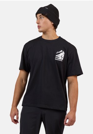 Zwarte katoenen t-shirt met een ronde halslijn en korte mouwen, met een witte grafische logo op de linker borst. Gecombineerd met een zwarte geribde beanie.