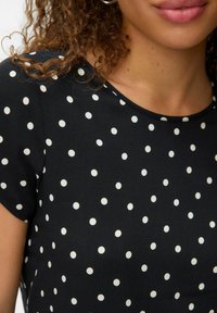 Zwarte top met korte mouwen en een ronde hals, met een patroon van witte stippen en een gladde, zachte textuur.