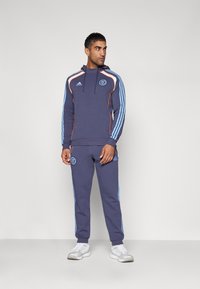 Set di felpa e pantaloni jogger navy con strisce arancioni e azzurro chiaro, dotato di un logo sul petto e sulla gamba sinistra dei pantaloni. Realizzato in tessuto morbido.