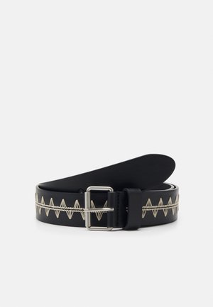Zwarte leren riem met zilveren gesp en beige zigzagstitch detail over de hele lengte, opgerold op een witte achtergrond.