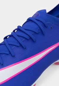 Μπλε ποδοσφαιρικό παπούτσι με υφασμένο συνθετικό επάνω μέρος, που διαθέτει ροζ και λευκές λεπτομέρειες στα πλευρά και παραδοσιακό σύστημα κορδονιών.