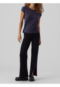 Top de manga corta en navy con un ajuste relajado, combinado con pantalones amplios negros con aberturas y un acabado texturizado. Zapatillas negras sin cordones.